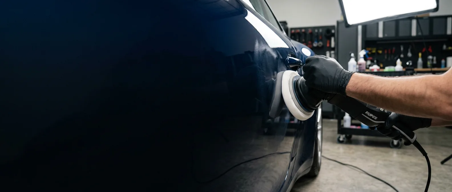 Dual-action polisher with foam cutting pad refining a glossy dark blue car panel under studio lighting at Brilliant Shine